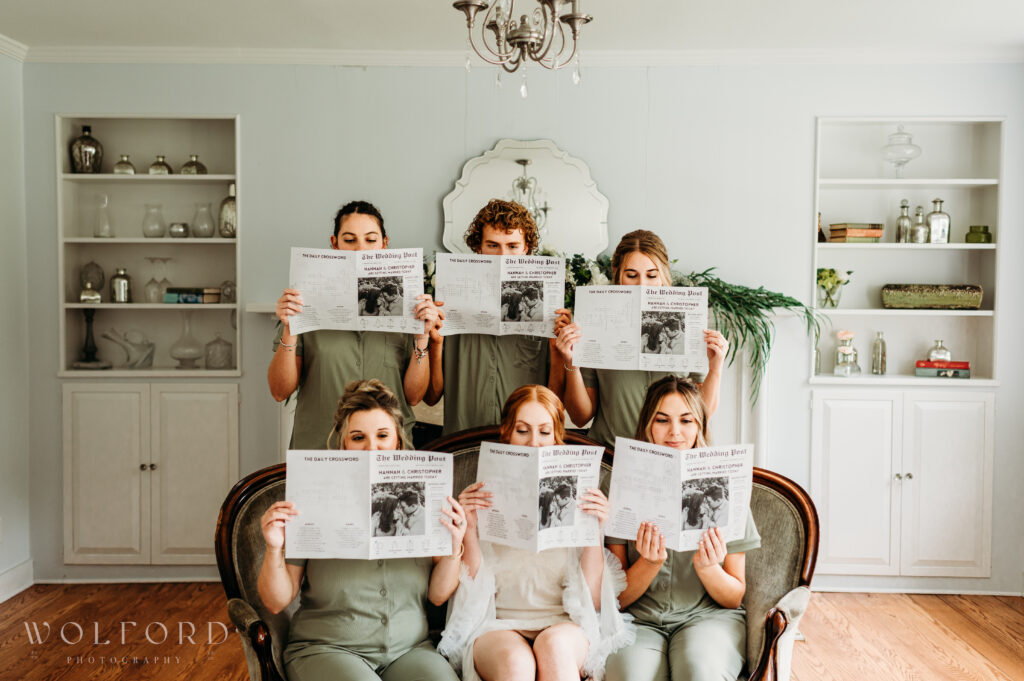 A group of bridesmaids pose together in matching pajamas, standing casually with playful expressions and relaxed postures. Some hold coffee mugs or champagne glasses, while others drape their arms around each other. The cozy setting reflects a fun and intimate moment shared during the wedding morning preparations, highlighting their close bond and excitement.